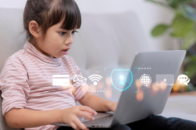 Child safety online Little girl using laptop at home icon of internet blocking app on foreground