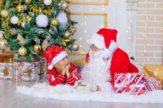 Bambino e babbo natale vicino all'albero di natale, il ragazzo guarda babbo natale