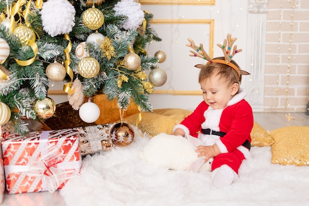 A child in a Santa costume sits at the Christmas tree with a rabbit, the concept of new year and Christmas