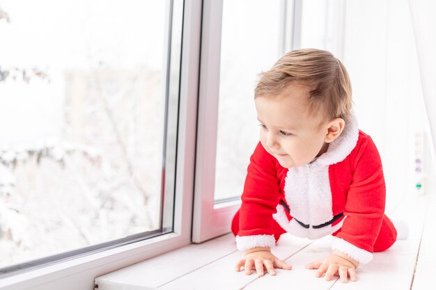 Bambino in costume da babbo natale sul davanzale della finestra, il concetto di nuovo anno e natale