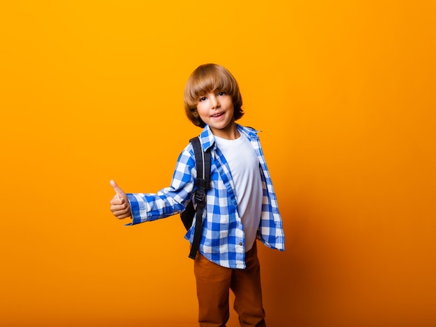 Child schoolboy boy showing thumbs up isolated on yellow background