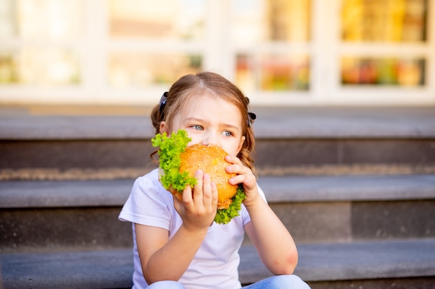 Photo a child schoolgirl eats lunch or a burger snack before school, a concept of back to school or feeding schoolchildren, close-up