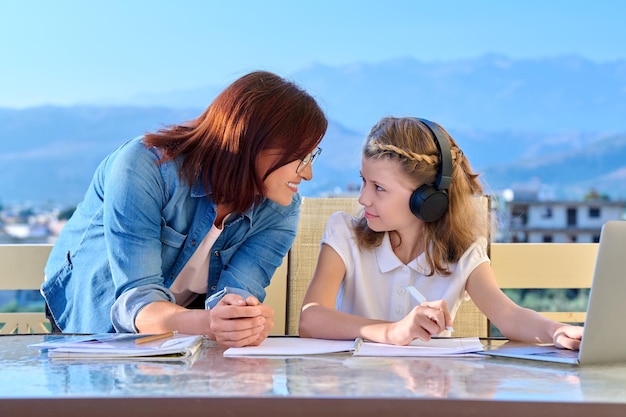 Child schoolgirl learns online with laptop mom helps