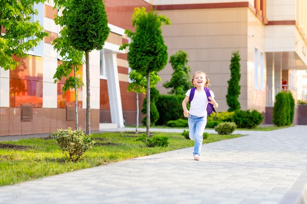 Foto una studentessa bambina con uno zaino salta di felicità e corre a scuola il primo giorno d'autunno, il concetto è tornato a scuola