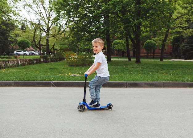 Child on a scooter in the park A little boy rides a scooter on a sunny day Active sports for preschoolers