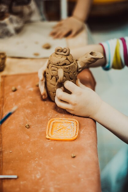 Child sculpts a small jar of wet clay