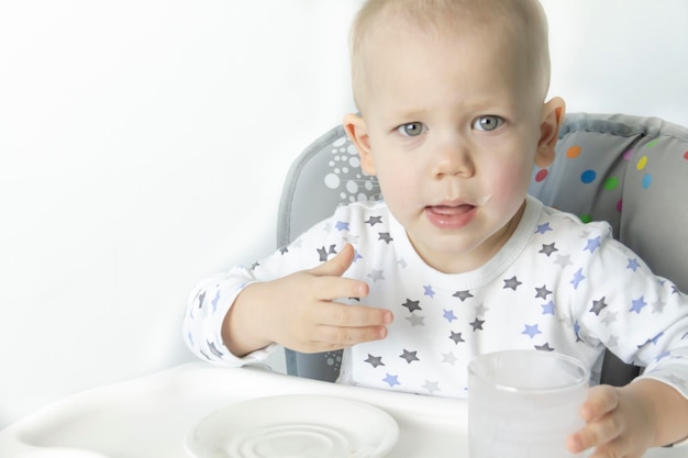 Детское кресло в пижаме со звездами пьет полезный йогурт на фоне белой стены