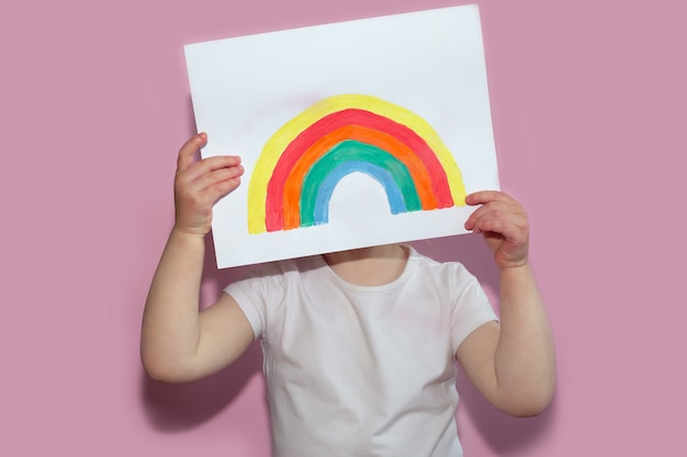 A child shows a drawing of a rainbow during pandemic coronavirus quarantine.