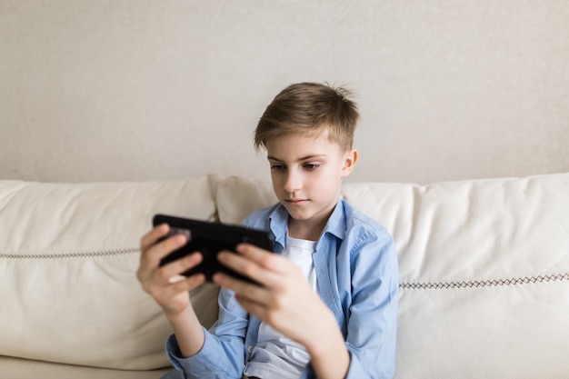 Child sit on the couch in his hands holding a phone plays with it