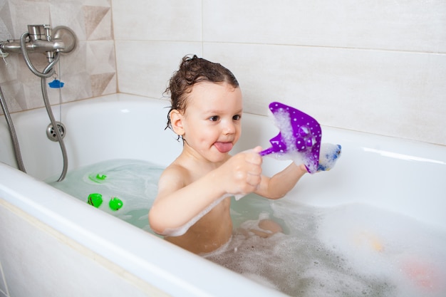 The child sits in a bath with water and plays with fish. Hygiene. Diving in a playful way.