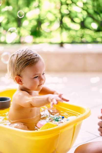 子供は水とおもちゃの入ったボウルに座って手を上げます