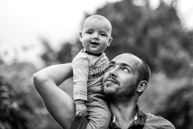 Il bambino si siede sulla spalla del papà e sorride. bianco e nero