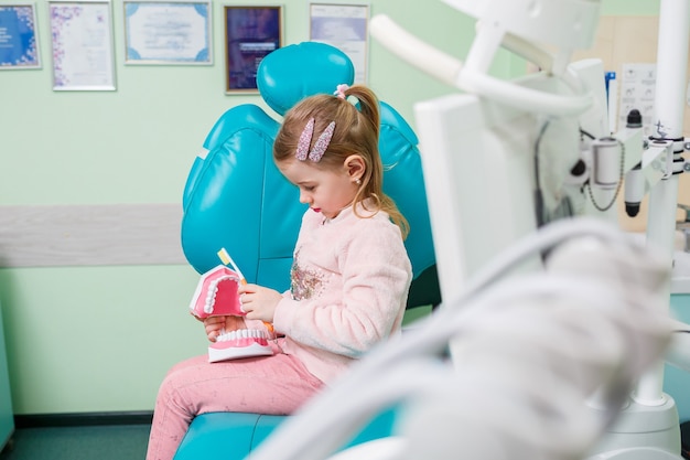 Photo the child sits in the dentist's office and holds an artificial jaw in his hands and brushes her teeth