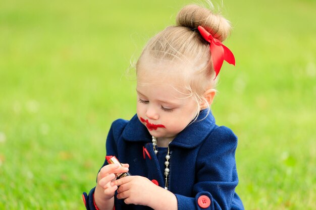 The child sits and paints his lips with red lipstick