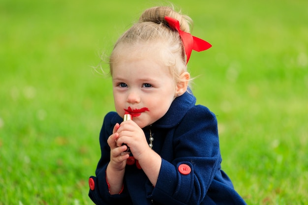 The child sits and paints his lips with red lipstick