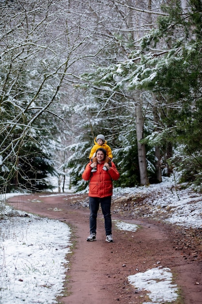 Child sits on the shoulders of his father during a walk by a frozen forest