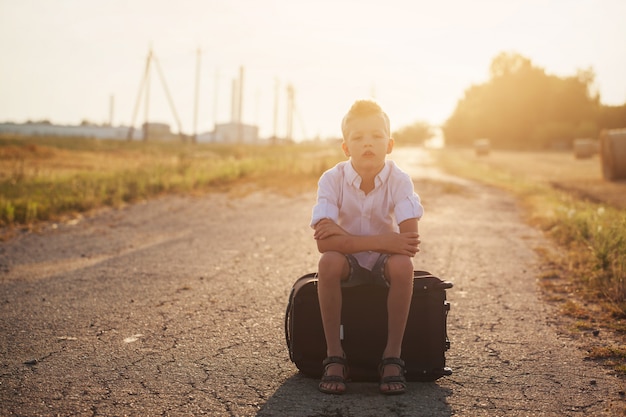 The child sits on a suitcase in the summer sunny day, the traveler