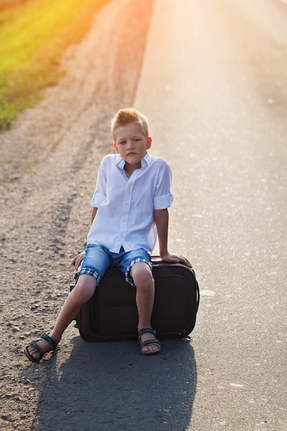 The child sits on a suitcase in the summer sunny day, the traveler