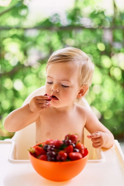 Child sits at the table and pulls a cherry into his mouth