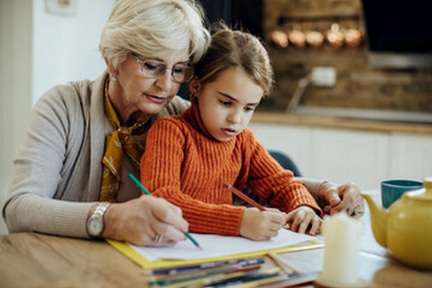 a child sits at a table with an older woman writing with an older woman