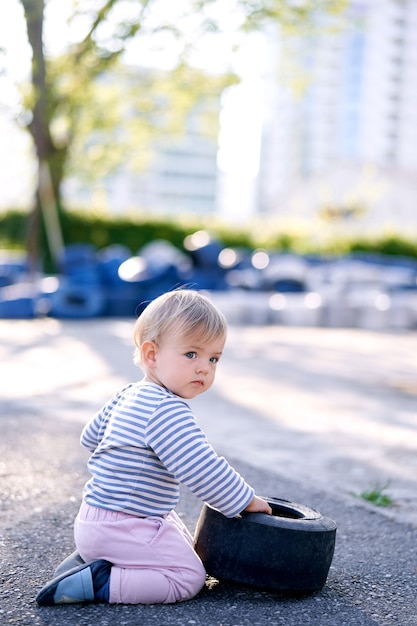 Child sits with his head turned and touches the rim of the car in the parking lot