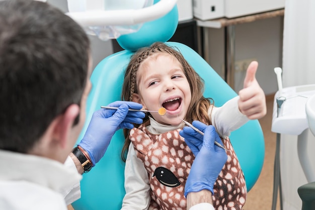 Child sitting in a dentist chair on the examination shows a thumb up