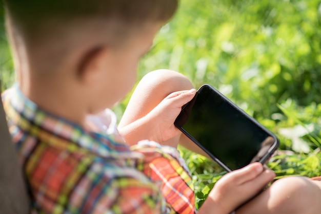 電話で見ている草の上に座っている子供