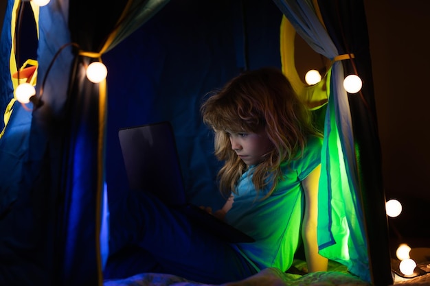 Photo child sitting in home tent playing with laptop