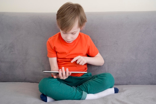 Bambino seduto sul divano e utilizzando la tavoletta digitale