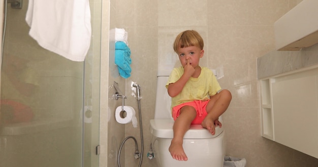 Child sitting toilet with thoughtful look picks his nose