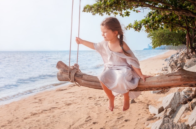 海沿いのビーチで木製のブランコに座っている子供