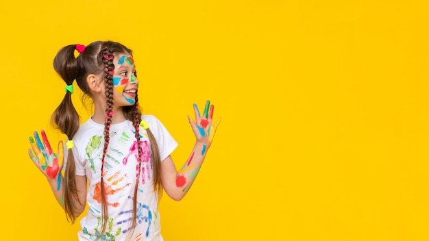 A child smeared with paint a little girl painted with multicolored paints points to your advertisement children's creativity yellow isolated background copy space banner