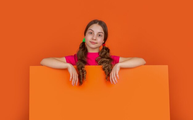 Child smile behind blank orange paper with copy space for advertisement