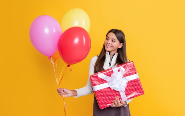 Child smile with party helium balloons and present box on yellow background