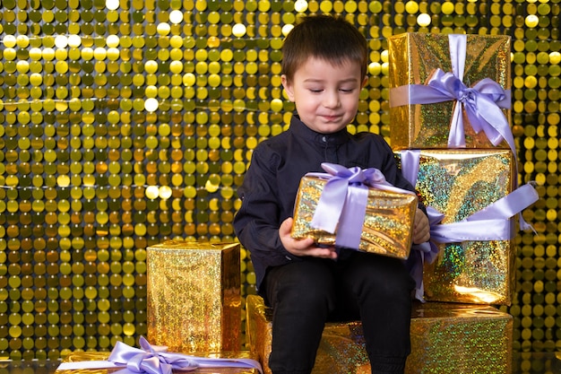 Child smiling boy holding gift box on background with gold shiny sequins paillettes