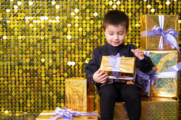 Bambino sorridente che tiene in mano una scatola regalo sullo sfondo con paillettes di paillettes dorate lucide