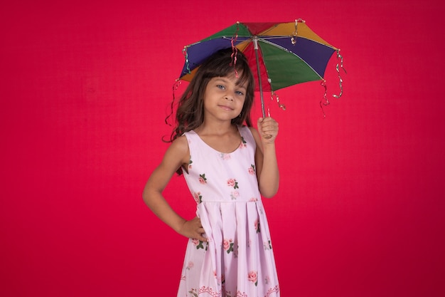 스튜디오 사진에서 화려한 우산을 들고 빨간색 배경을 가진 아이가 웃고 있습니다.