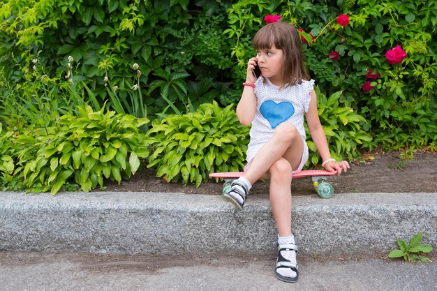 The child speaks on the phone while sitting on a skateboard