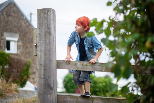 A child stands on a fence in front of a house.