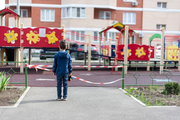 A child stands over a playground fenced with red ribbon holds a toy car in his hand