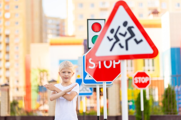 A child stands at a STOP sign and holds his hands in a cross