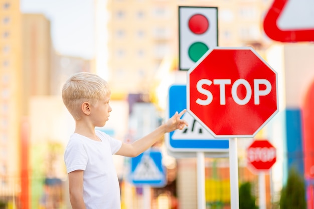 A child stands at a stop sign and holds his hands in a cross