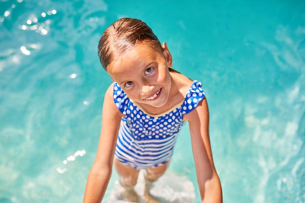 A child on the steps climbing out of the pool, little girl having fun in the swimming pool, summer vacation at home, tropical holiday resort.