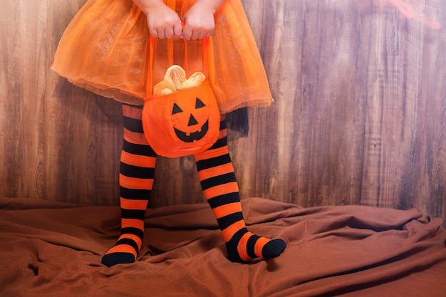 Child in striped leggings with a pumpkin bag for Halloween sweets