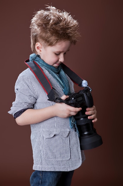 Child in studio with professional camera. Boy is using a camera on brown.