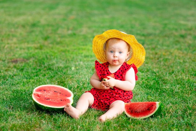 A child in the summer on the green grass eats a watermelon in a yellow hat space for text