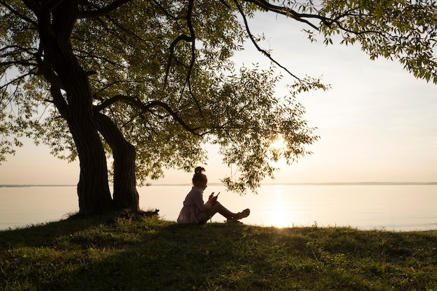 A child at sunset sits under a tree beautiful artistic photo with a kid girl in nature on a sunny su...