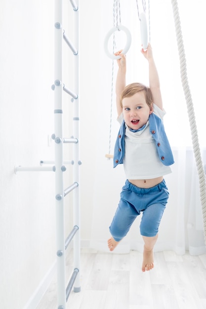 Ребенок на шведской стене занимается спортом дома мальчик поднимается по лестнице с веревкой концепция спорта и здоровья