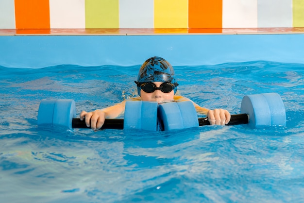 Photo child swimming with a water dumbbells in hand in swimming pool