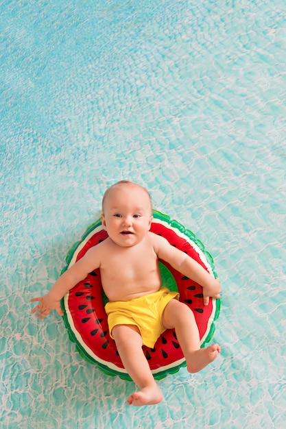 child swims in a lifebuoy of a watermelon near a sandy beach with palm trees on the seashore